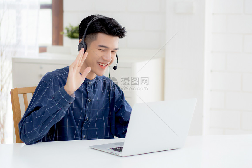 从事膝上型计算机工作在家戴耳机的年轻亚洲商人身戴头盔的商人负责电视会议通信和教育男学习和电子图片