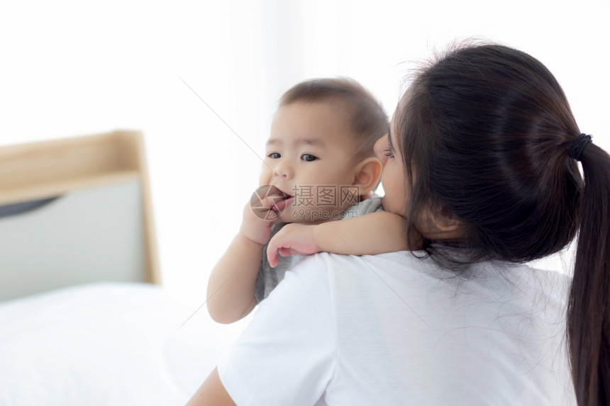 年幼的母亲把小女婴放在家中的卧室里母亲带着孩子和照顾妇女孩子无忧虑幼儿和父母情感表达家庭概念图片