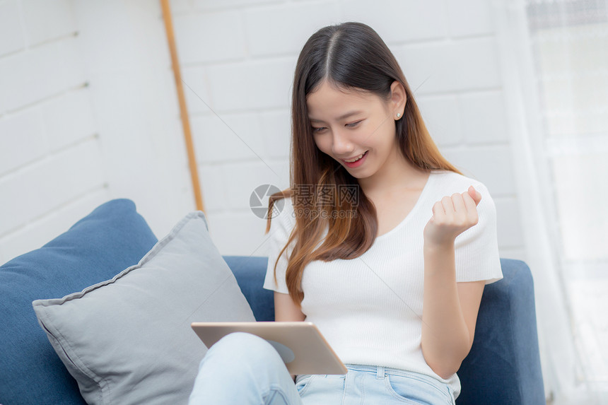 在家沙发上使用浏览平板电脑休息的年轻有吸引力女坐在沙发上的快乐女孩坐在沙发上放松阅读数字工具图片