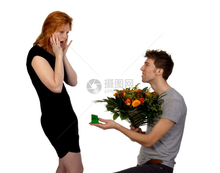 年轻男人给他惊讶的女朋友一大束花和一枚戒指孤立在白色背景上图片