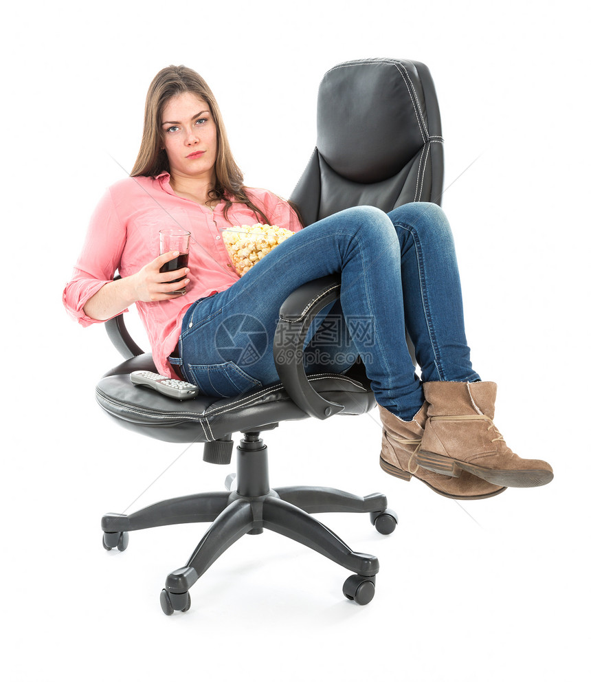 坐在椅子上拉伸的懒女人带着爆米花和一杯饮料与白色隔绝图片