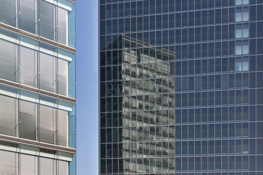 两座现代办公大楼其中一栋在另的玻璃面墙上反射另一栋大楼的玻璃面墙上反射的办公大楼图片