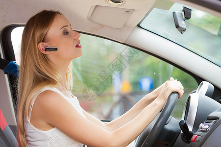 年轻金发女青年用手机和头盔驾驶汽车侧视妇女用耳机驾驶汽车图片