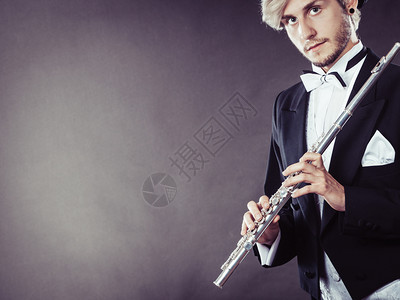 古典虚拟演播室古典音乐激情和爱好概念穿着优雅音乐的金发年轻男子拿着长笛的肖像深灰色背景的演播室拍摄穿着优美服装的音乐家拿着长笛背景