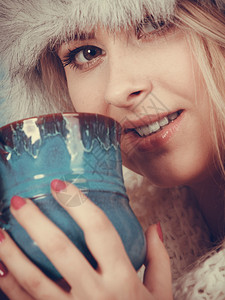 时装概念冬的金发女人喝杯茶热饮蓝背景黄发女人冬的金毛帽子喝酒图片