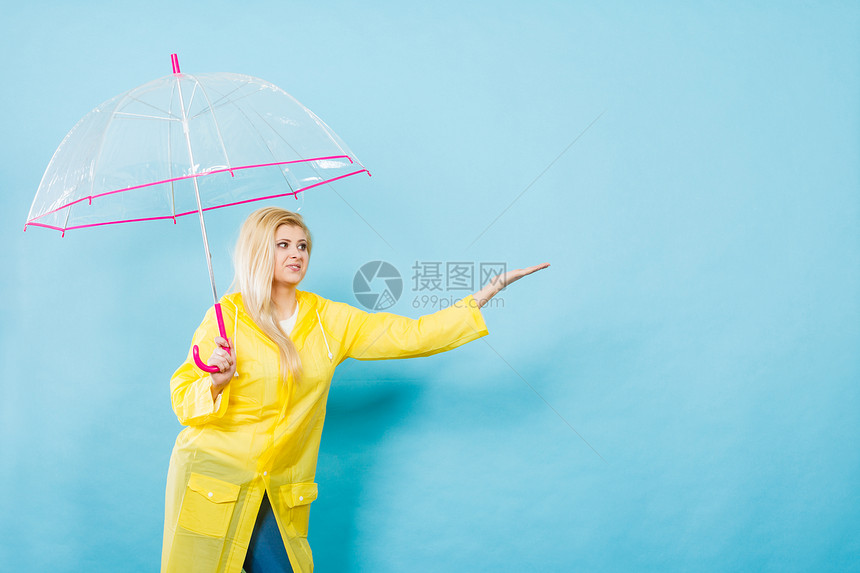 身穿黄色雨衣的金发女人拿着透明的雨伞检查天气是否下雨图片