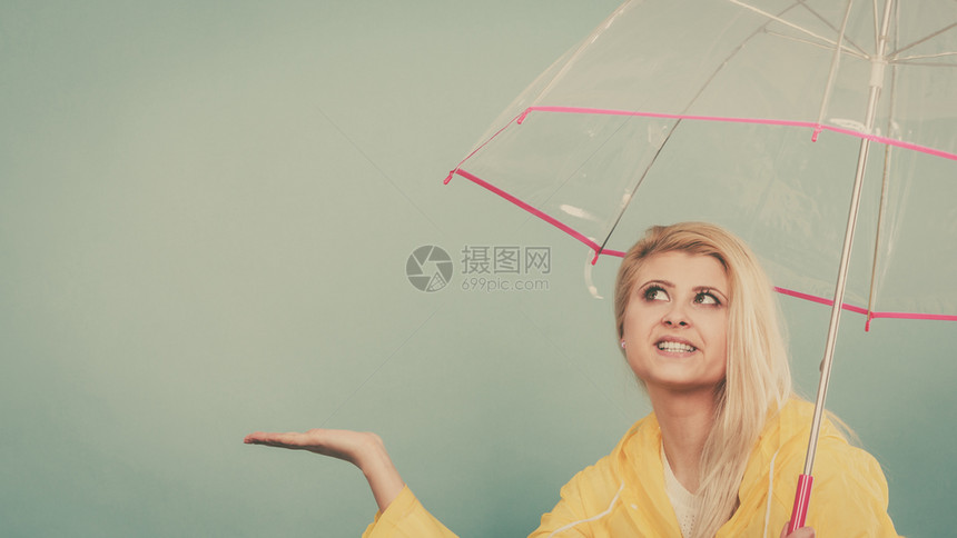 身穿黄色雨衣的金发女人拿着透明的雨伞检查天气是否下雨图片