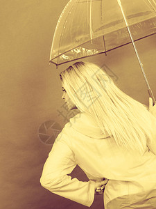 穿着雨衣的金发女人拿着透明的雨伞检查天气是否下雨图片