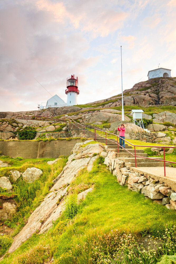 游客妇女和历史上的红白灯塔在岩石海岸的边缘南挪威林德斯内斯Fyr灯塔挪威的林德斯内斯灯塔图片