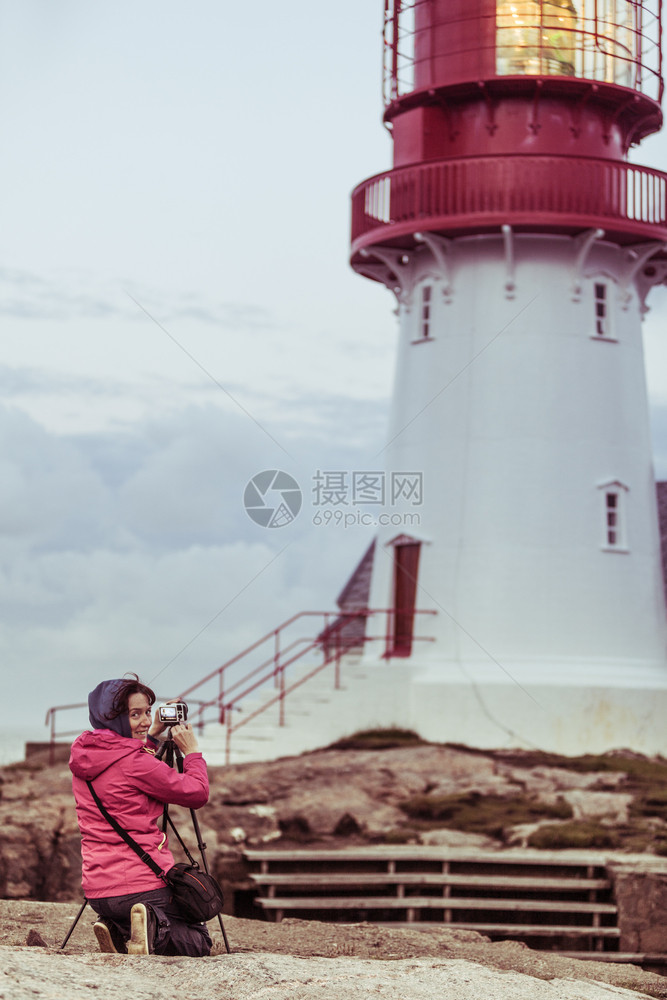 女旅游客行者在挪威南海岩石岸边缘历史红白灯塔拍照LindesnesFyr灯塔挪威林德森灯塔旅游者图片