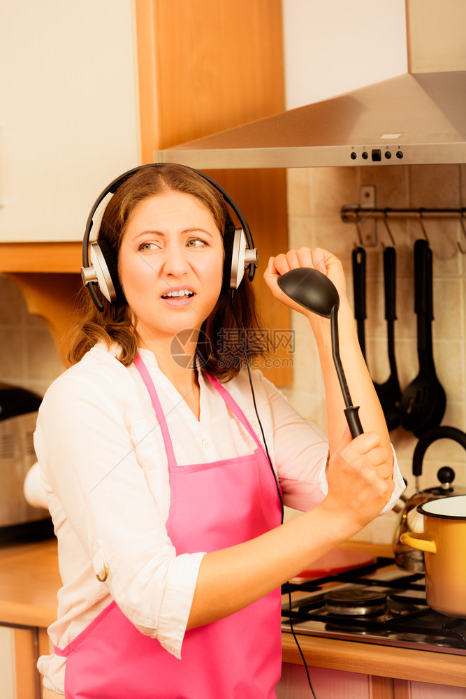 现代女家庭主妇烹饪厨师穿着粉红色围裙在厨房听耳机唱歌和跳舞时听音乐图片