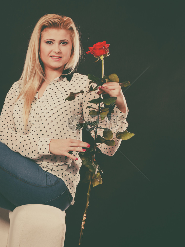 美丽的金发女人坐在白沙上拿着红玫瑰在黑暗中坐沙发上的女孩拿着红玫瑰在黑暗中图片
