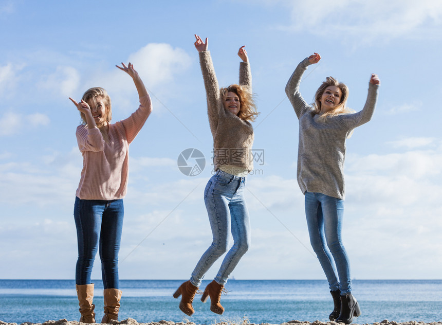 三个充满欢乐的女人带着天空在背景中跳来去女朋友在户外玩去三个女在外跳来去图片