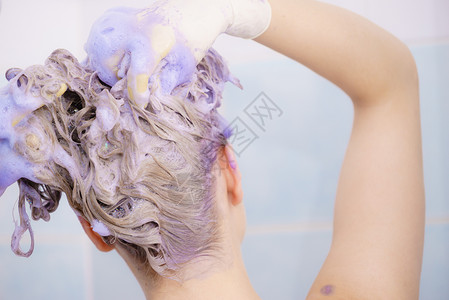 女在头发上涂彩色洗水女有紫色洗发制品在家里染金色女在头发上涂彩色洗水背景图片