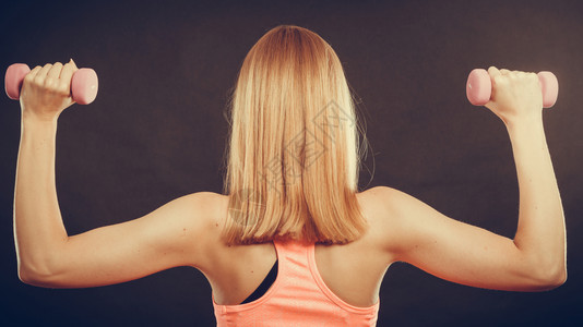 强壮的金色发美女举起重量背影制片厂拍摄在黑色背景上图片