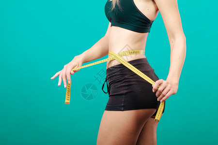 体瘦健康的生活方式概念身体健康的女孩用绿色测量胶带她的腰围身体健康的女孩测量她腰围背景图片