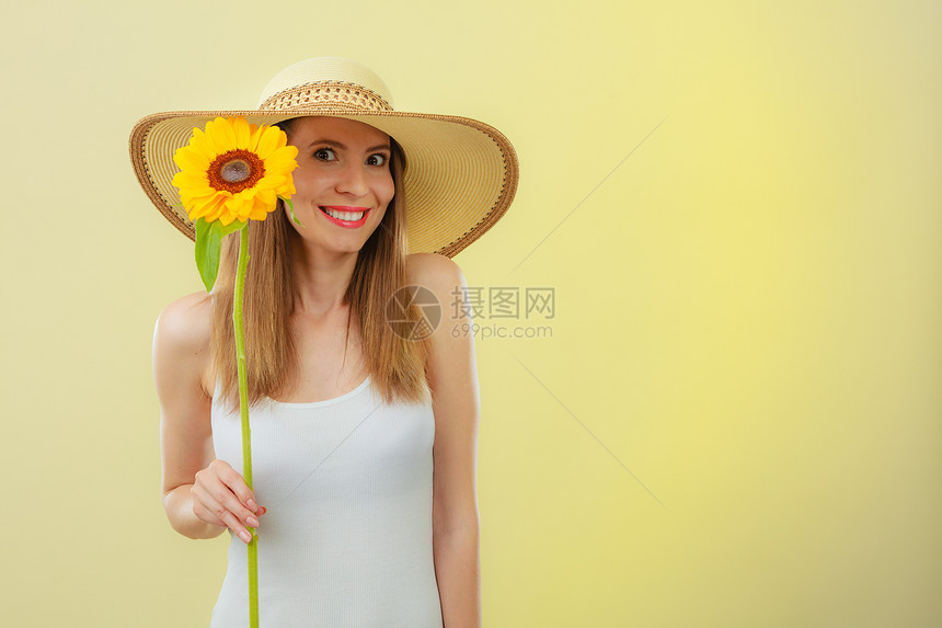 穿着草帽的有吸引力夏日女子特写肖像黄色背景的向日葵手握着图片