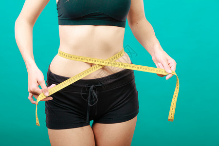 体瘦健康的生活方式概念身体健康的女孩用绿色测量胶带她的腰围身体健康的女孩测量她腰围背景图片