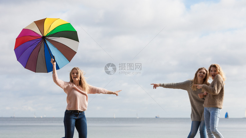 带着五颜六色雨伞的女人她的两个朋友在取笑她取笑她女人取笑跳朋友图片