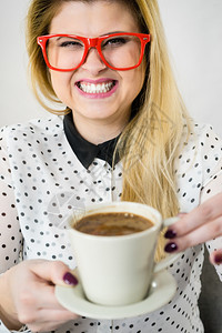 快乐的年轻女子在办公室戴着眼镜喝热咖啡或茶享受工作期间的休息时图片