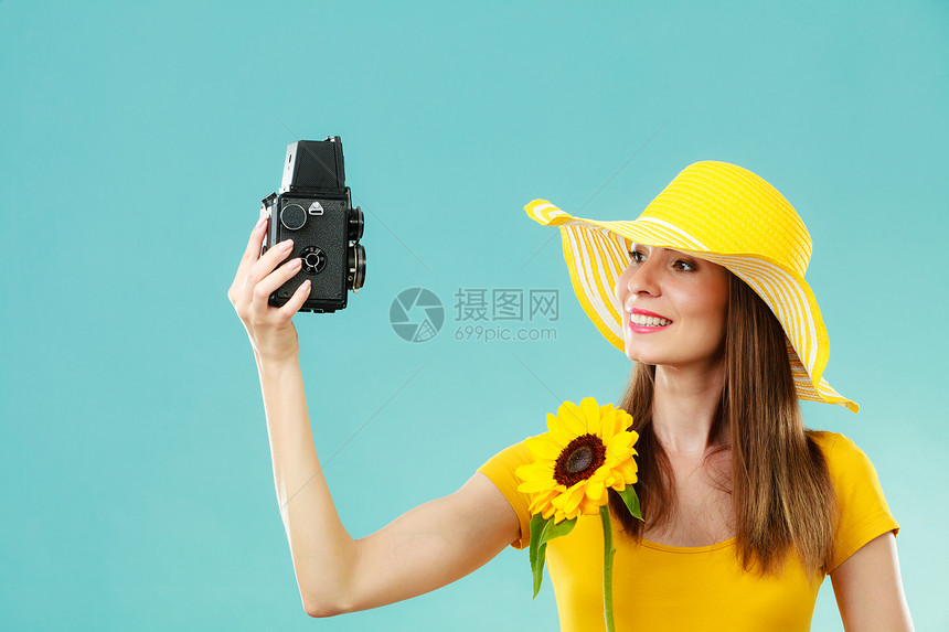 身穿黄色礼服戴向日葵帽子的暑期妇女用蓝色背景的旧相机自拍图片
