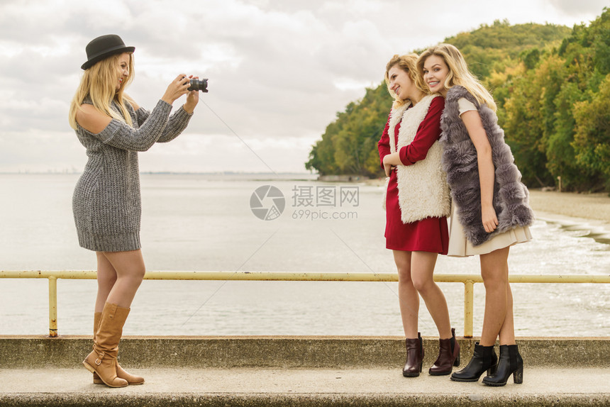 三名女朋友在户外拍照时玩得开心女在温暖的秋天气中拍摄两个照片时装模特的照片拍摄图片