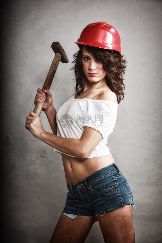 别平等和女权主义戴安全头盔的感女孩在灰色上拿着锤子工具年轻有吸引力的建筑工人作室中图片