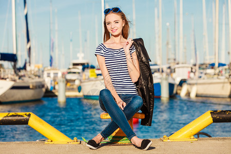 时装金发女孩蓝色心型太阳眼镜在码头对港口的游艇背景图片