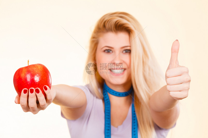美食健康品水果概念金发女人脖子上挂着测量胶带拿大红苹果举起拇指手势红苹果健康食品概念图片