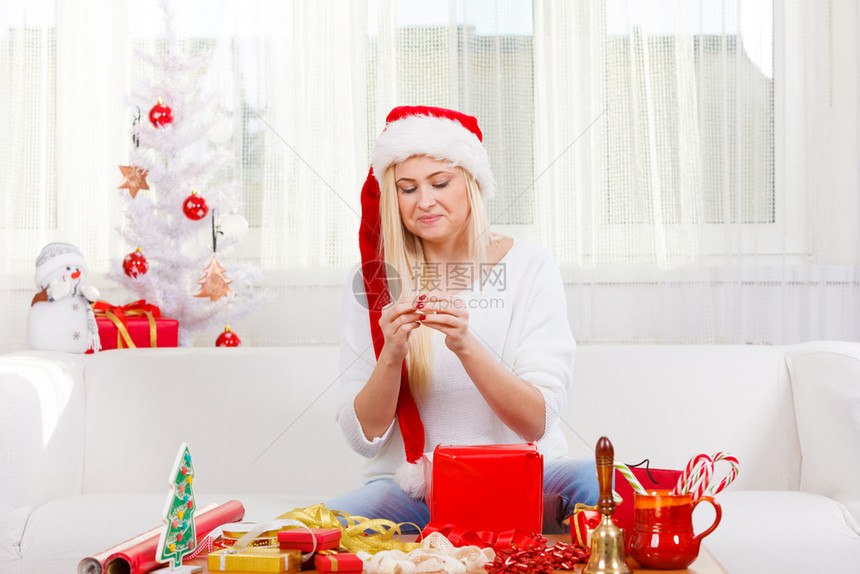 节日礼物季节概念戴圣诞帽的女人坐在沙发上打开圣诞礼物戴圣诞帽的女人打开圣诞礼物图片