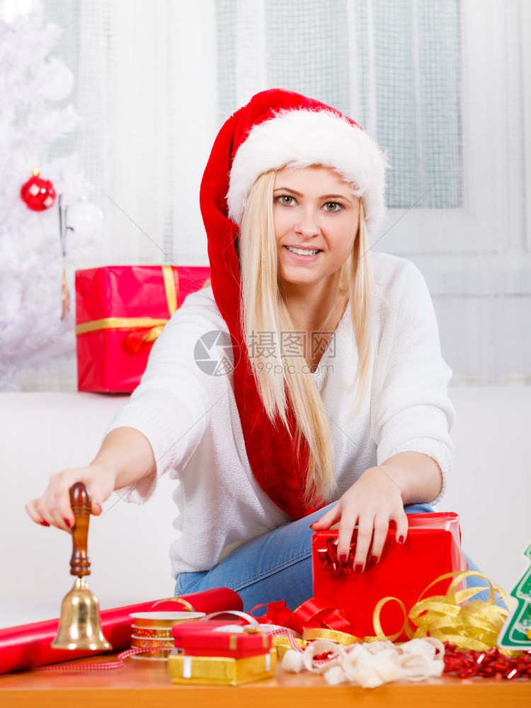 节日礼物季节概念戴圣诞帽的女人坐在沙发上准备和打包圣诞礼物戴圣诞帽准备圣诞礼物的女人图片