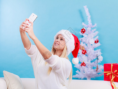 现代假日概念穿着圣诞礼帽的金发女人给自己拍圣诞照用智能手机自拍图片