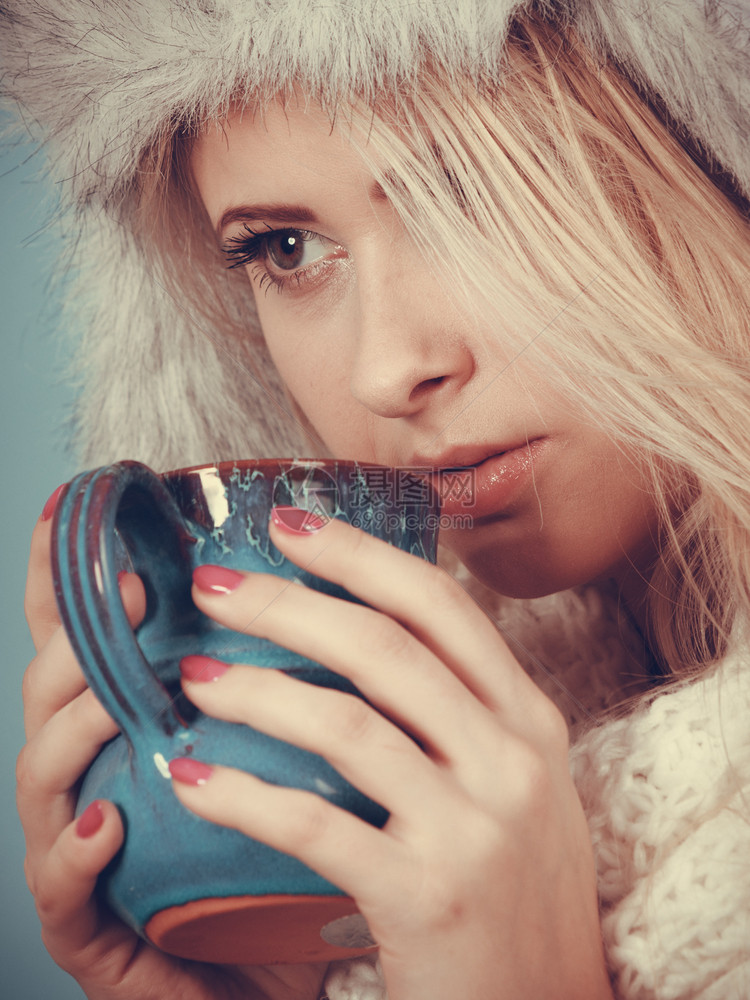 时装概念冬的金发女人喝杯茶热饮蓝背景黄发女人冬的金毛帽子喝酒图片