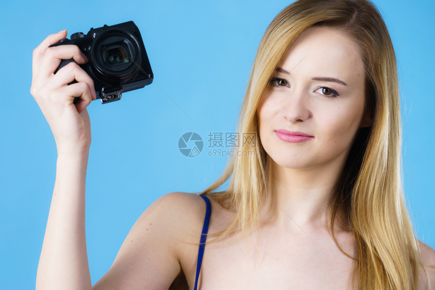 年轻女拿着旧式模拟相机拍照工作室摄的是蓝背景年轻女拿着旧式相机图片