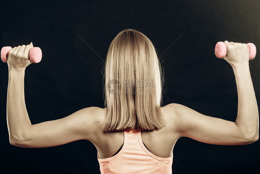 强壮的金色发美女举起重量背影制片厂拍摄在黑色背景上图片