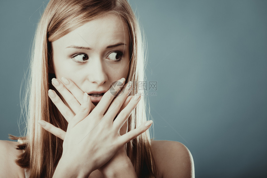 紧闭的年轻惊异女人眼睁地用蓝色的手把嘴罩在上图片