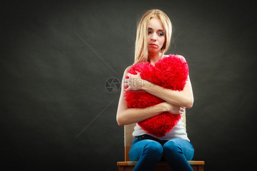伤心的坐在椅子上抱着红心枕头的不开女人黑暗背景图片