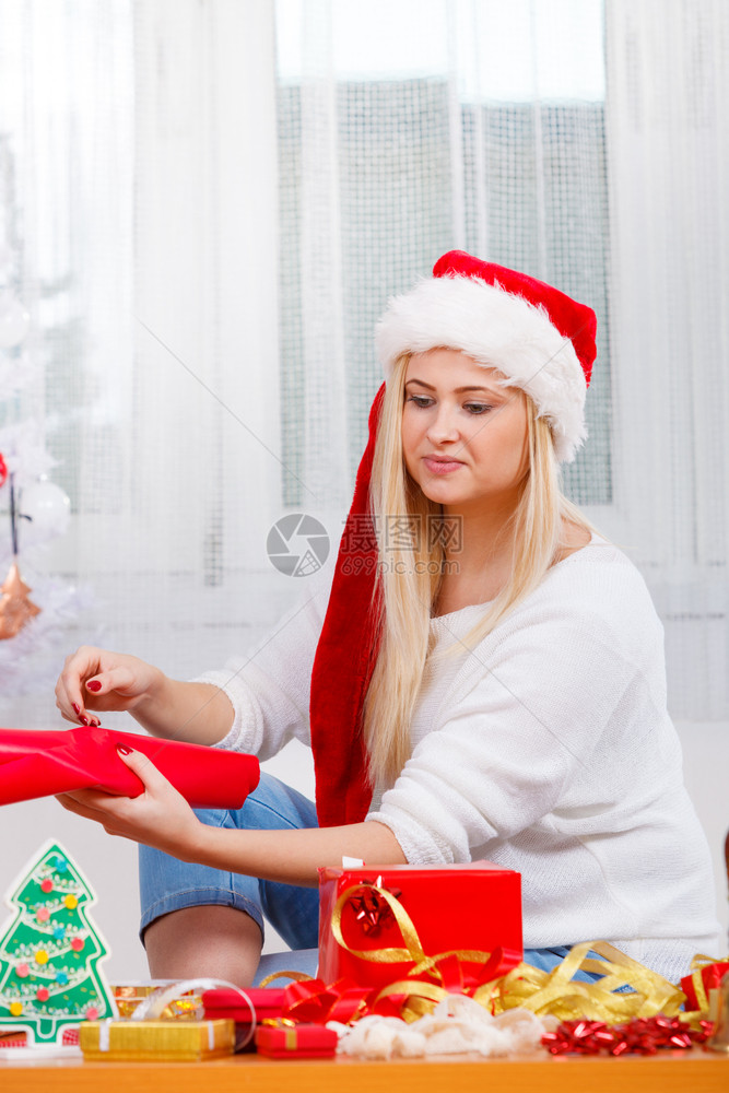 节日礼物季节概念戴圣诞帽的女人坐在沙发上准备和打包圣诞礼物戴圣诞帽准备圣诞礼物的女人图片