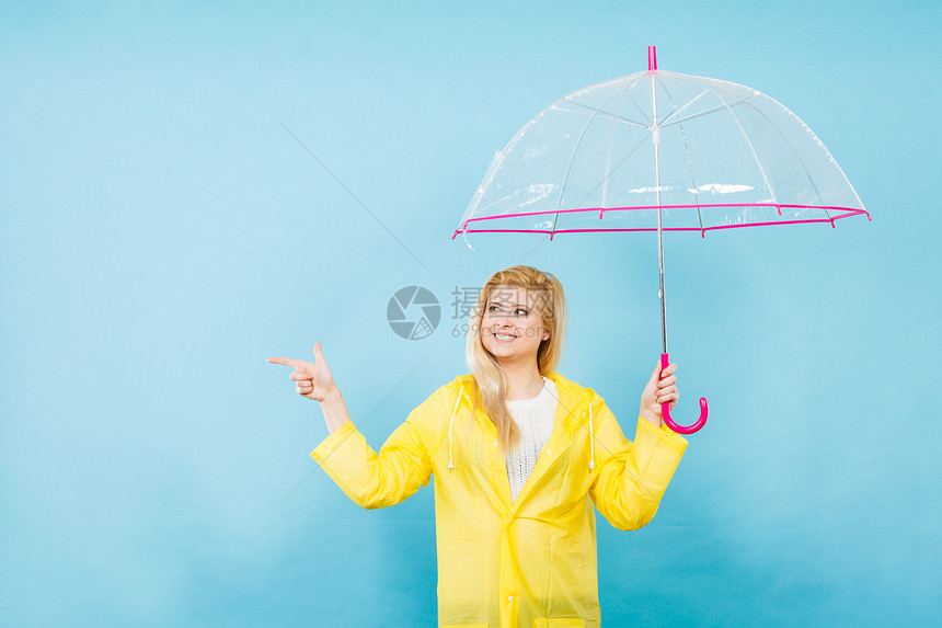 身穿黄色雨衣的金发女人拿着透明的雨伞检查天气是否下雨图片