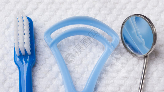 蓝色镜子口腔卫生保健概念关闭牙科工具蓝刷镜子和白毛巾上的舌清洁剂背景
