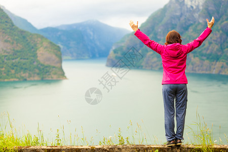 旅行概念自由游妇女快乐享受手举起来望着挪威的fjords山在挪威的Norwegian山码头举起手来的妇女背景