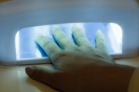 妇女手在UV红灯烘干指甲加凝胶混合修美体水疗处理概念图片