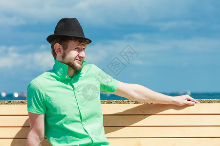 暑假和放松的概念坐在海边的长椅上的时髦小伙子图片