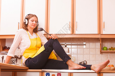 准备食物概念听音乐深思熟虑的家庭主妇用耳机做厨师家里有黄色围裙图片