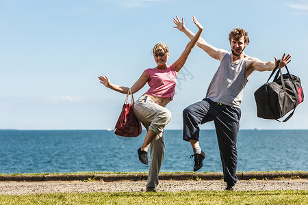一对幸福的情侣带着运动健身包在海边户外活泼的年轻女孩和穿着运动服的男孩举起手来幸福带着运动包的幸福夫妻背景图片