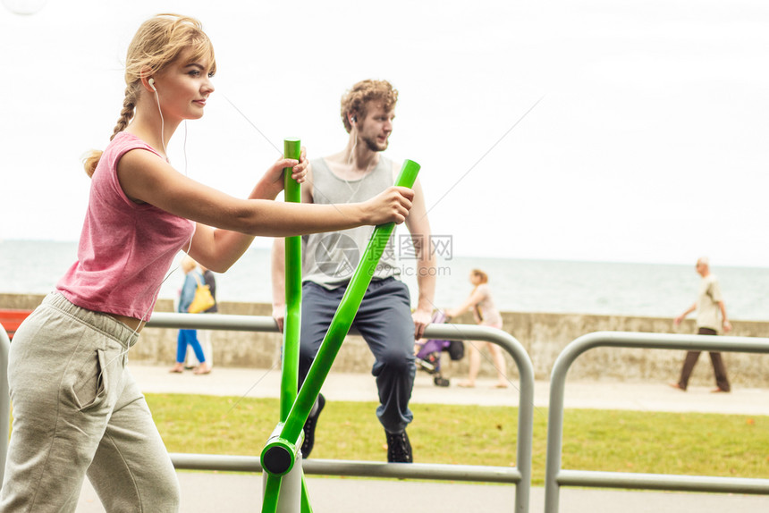 活跃女在体操机上锻炼男在户外健身房听音乐体育健身男女在体操教练上锻炼图片