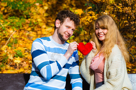 年轻夫妇坐在公园的长椅上抱着心笑分享美好的情感背景图片