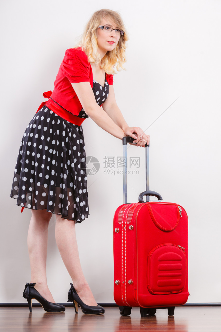 旅行度假概念身穿波尔卡圆点黑色高跟鞋准备出行的红色手提箱全身穿着波尔卡圆点黑衣服的优美年轻女子图片