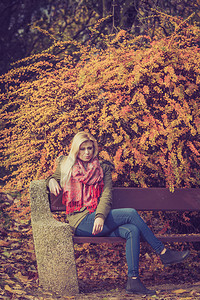 秋天气下妇女坐在公园的长椅上休息黄金季节假是背景图片