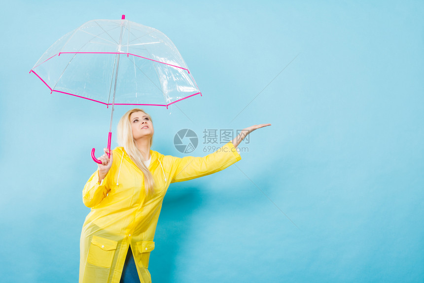 身穿黄色雨衣的金发女人拿着透明的雨伞检查天气是否下雨图片